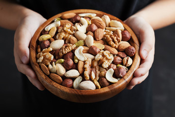 Childrens hands holding a wooden bowl with mixed nuts. Healthy food and snack. Walnut, pistachios,...