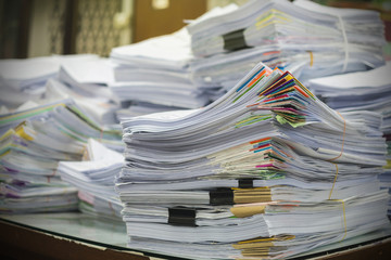 Pile of documents on desk stack up high waiting to be managed.