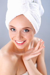 Beautiful young woman applying a creme on her face isolated on gray background