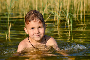 Fototapeta premium Boy swims in the lake water with a green tint.