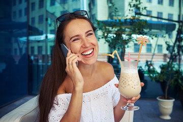 Smiling woman drinking cocktail in outdoor café and chatting on