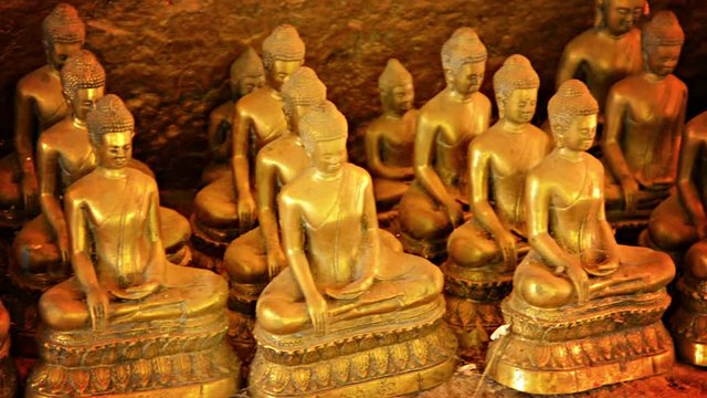 Video 1080p - Panning from left to right across a collection of near-identical Buddhist statues in a village in Cambodia. Sculptures are gold-colored, and appear to be arranged in a cave
