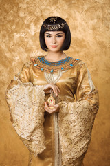 Beautiful Egyptian woman like Cleopatra with perfume bottle on golden background