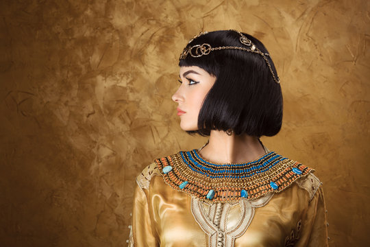 Beautiful woman like Egyptian Queen Cleopatra on golden background. Side view, face profile