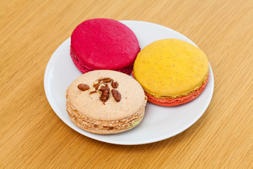 Three traditional french colorful macarons on plate, wooden background
