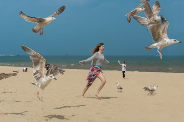 Young woman dancing with seagulls on the beach