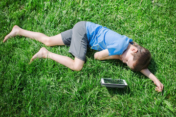 boy fell asleep on the grass with tablet. child sleeping on the grass under the sun after a play on the digital tablet. view from above