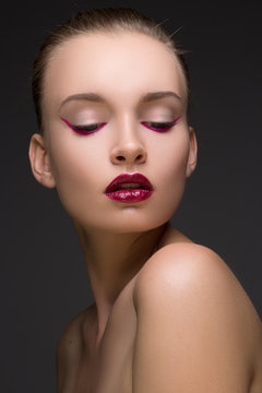 Fashion portrait of perfect woman with red or maroon lips and magenta arrows bottom of eyes on dark gray background.