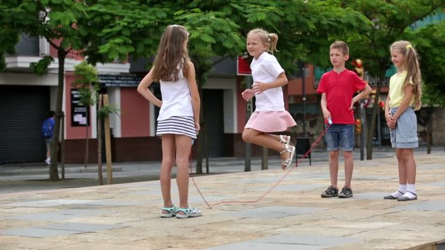 Smiling kids in school age playing together with jumping rope outdoors


