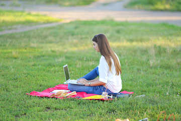 young girl sitting in the park and talking with headphones on Skype through the notebook. student...
