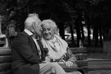 Old man and old woman talking on a park bench. Black and white.