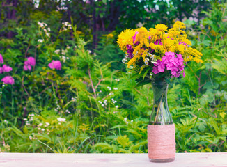 Fototapeta premium a bouquet of flowers of goldenrod, Phlox and chrysanthemums in a glass bottle on a natural background. tinted photo