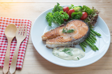 Fried salmon with vegetable on a round white plate on wooden bac
