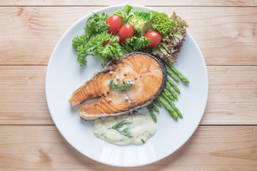 Fried salmon with vegetable on a round white plate on wooden bac