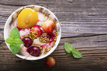 Healthy breakfast snack. Marble Portion bowl full of cherry smoothie with natural yogurt, ripe berries, fruits, bee pollen, berry syrup on a wooden background