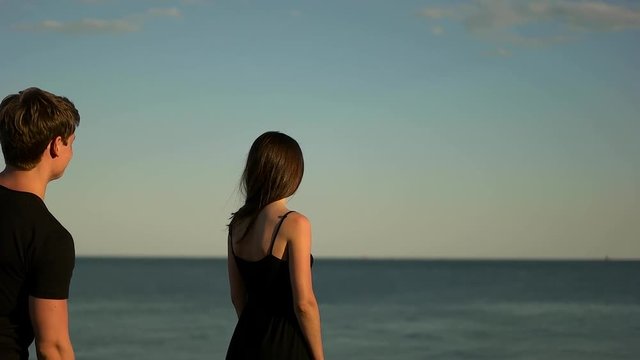 Guy hugs a girl in black by the sea.