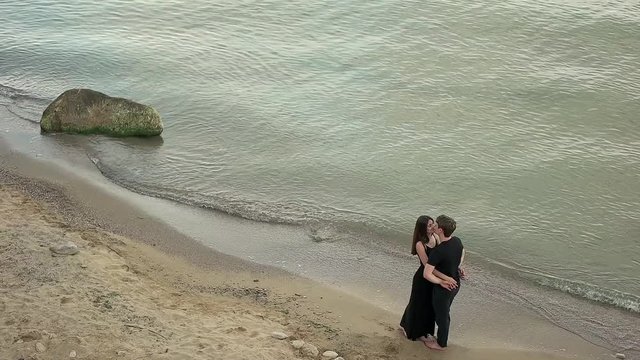 Couple in black clothing embracing by the sea.