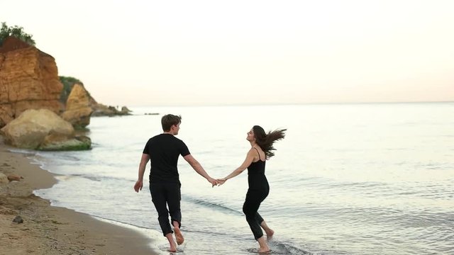 Couple running holding hands barefoot on the beach.