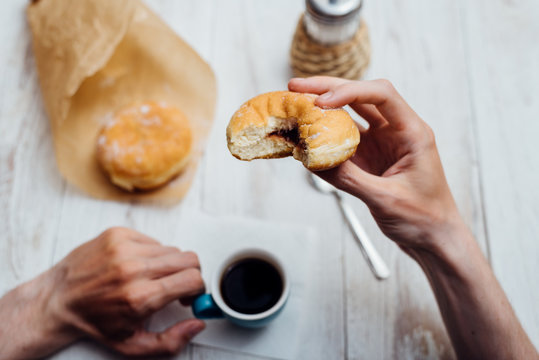 Man hands eating Bismarck donut with coffee on wooden table
