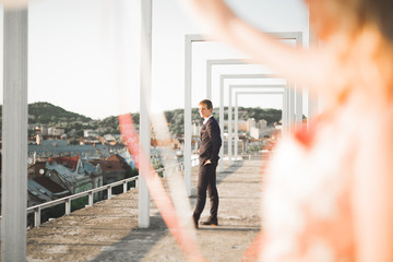 Pretty sunny outdoor portrait of young stylish couple while kissing on the roof with city view