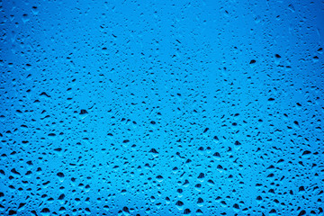 Water drops flow down on the glass in the rain, on a blue background