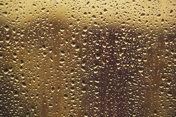 Water drops flow down on the glass in the rain, on a yellow back