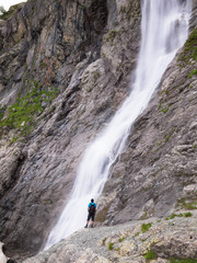 Obraz premium Adult male with a backpack standing lonely on the edge of the cliff and looking at the big waterfall
