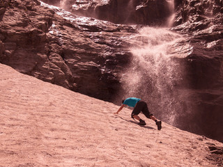 Toned image of an adult male to climb the mountain through the snow against the backdrop of a large waterfall