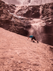 Toned image of an adult male to climb the mountain through the snow against the backdrop of a large waterfall