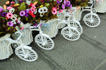 Fototapeta na wymiar small toy bicycle with flowers in a basket on a cobblestone street. Postcard Greetings