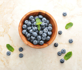 Fresh blueberries with mint leaves in a wooden bowl on a marble