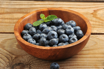 Fresh blueberries  in a wooden bowl with mint leaves on wooden b
