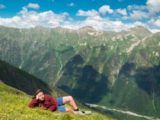 Young woman lying in a meadow with flowers in front of the North Caucasus mountain range with the sky and clouds
