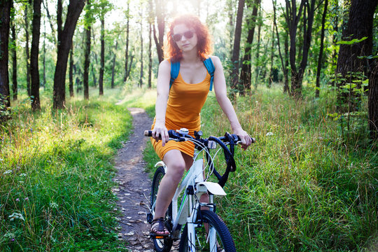 Young redhead woman in sunglasses riding a bike in the city park