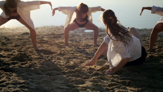 Dance performance of four girls on sand beach near lake at dawn