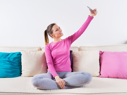 young attractive girl playing on home sofa couch taking selfie portrait with mobile phone having fun laughing and smiling happy and playful