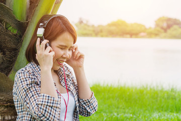 Relaxed young woman listening to the music with headphones lying on the green grass