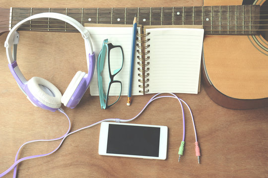 Concept song composer.Notebook pencil smartphone glasses guitar on the wooden floor.Process in vintage color tone