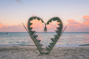 Naklejka premium Palm branches tied into the shape of a heart on the beach.