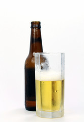 A glass of beer with the brown beer bottle in the background.
