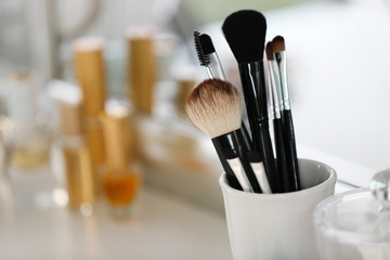 Cosmetic brushes in cup on light blurred background