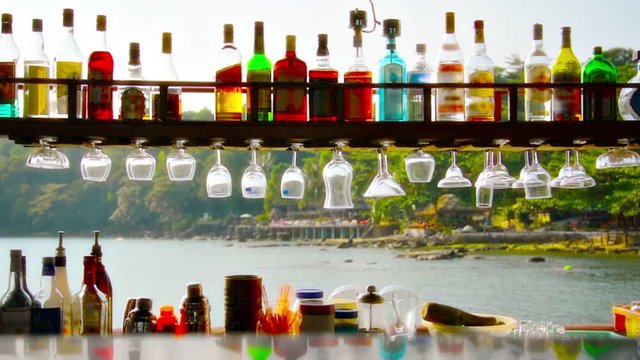 Looking out a beautiful, tropical beach in Sihanoukville, Cambodia from behind a seaside bar. Colorful liquor bottles and glasses displayed in foreground.