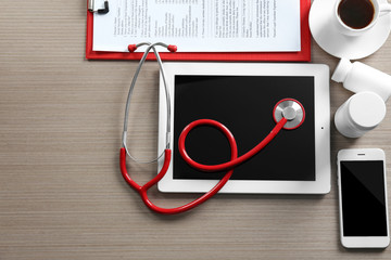Red stethoscope with tablet and accessories on wooden table