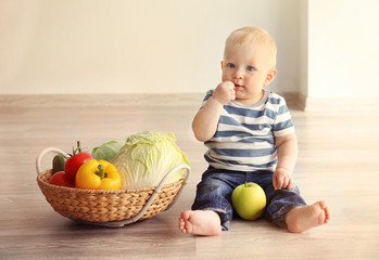 Fototapeta premium Cute baby and fresh vegetables in wicker basket on wooden floor