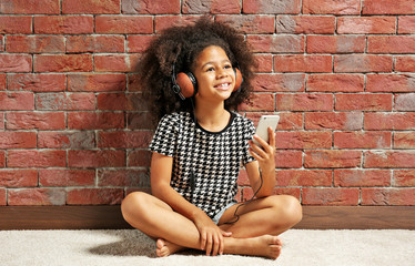 Afro-American little girl with headphones on brick wall background