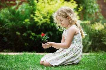 Little blonde girl holding young flower plant in hands on green background