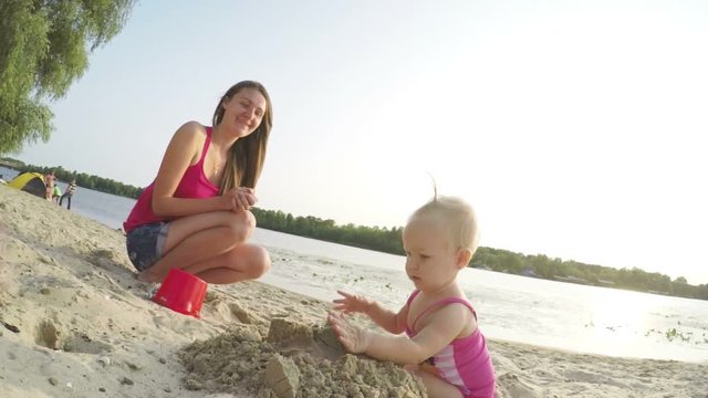 Baby girl having fun and destroys sand figures on the beach