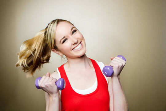 Happy fit woman lifting dumbbells smiling and energetic.