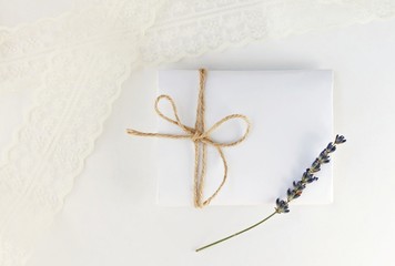Soft romantic background. White paper envelope gift with twine bow, dried lavender flower, blur lace. Light delicate mockup.