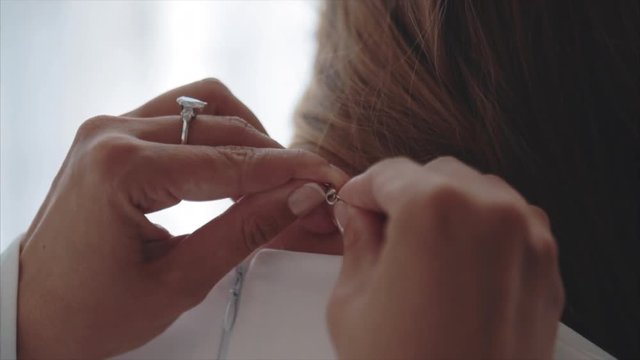 mother helps to put on a white dress, clasps a chain on the daughter
